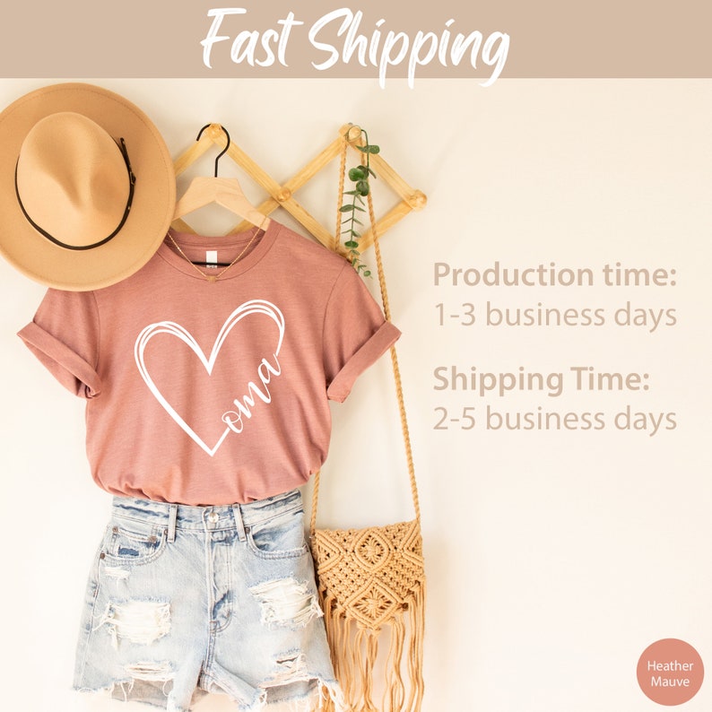 Pu&ograve; includere: Una t-shirt color malva con un cuore bianco e la parola "oma" al suo interno. La t-shirt &egrave; appesa a un appendiabiti di legno con un cappello di paglia e una borsa intrecciata.