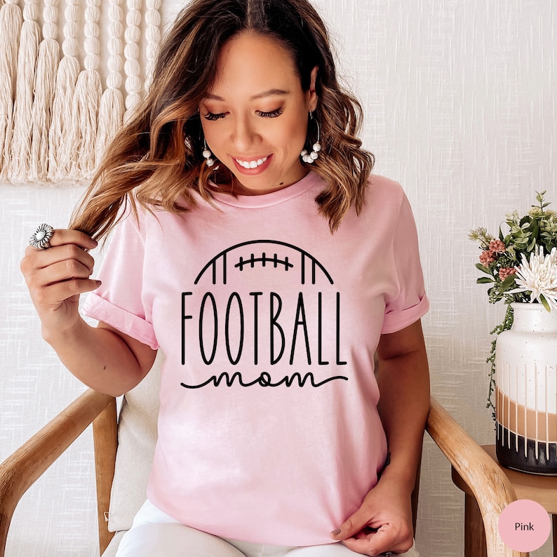 May include: A pink t-shirt with a black graphic of a football and the text "FOOTBALL mom".