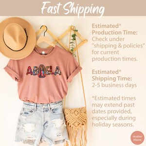 May include: A heather mauve t-shirt with the word "ABUELA" in colorful mosaic letters. The shirt is hanging on a wooden rack with a straw hat and a woven bag. The text "Estimated* Production Time: Check under "shipping & policies" for current production times. Estimated* Shipping Time: 2-5 business days *Estimated times may extend past dates provided, especially during holiday seasons. Heather Mauve" is visible on the right side of the image.