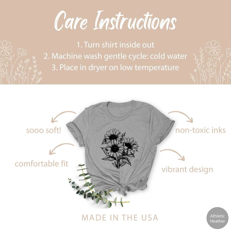 May include: Athletic Heather gray t-shirt with a black sunflower design. The shirt has the text "Care Instructions" and "MADE IN THE USA". Additional text includes "sooo soft!", "comfortable fit", "non-toxic inks", and "vibrant design".