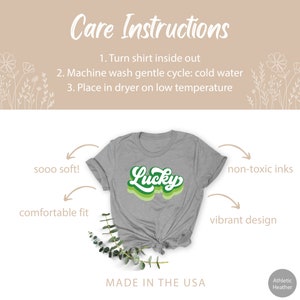 May include: A gray t-shirt with a green and white "Lucky" graphic. The shirt is made with soft, comfortable fabric and features non-toxic inks. The design is vibrant and the shirt is made in the USA.