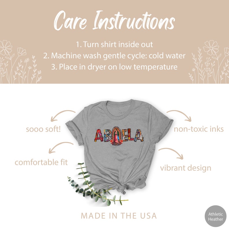 May include: A gray t-shirt with the word "ABUELA" spelled out in colorful mosaic letters. The letters are decorated with images of flowers, birds, and a religious figure. The shirt is made in the USA and features a comfortable fit, soft fabric, and non-toxic inks.