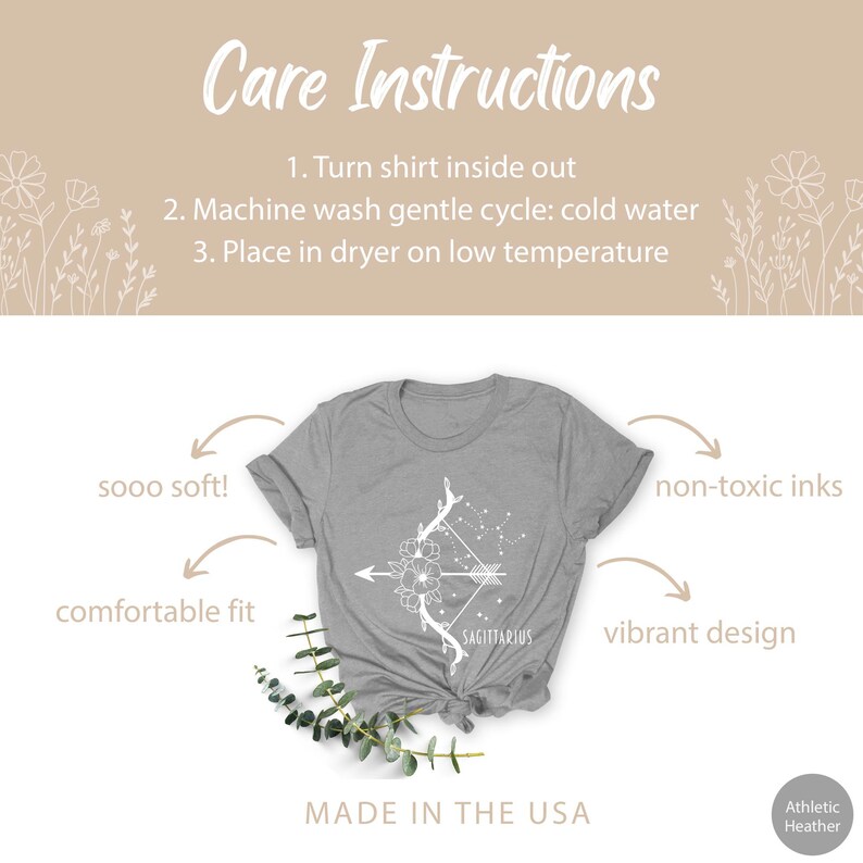 May include: Grey t-shirt featuring a white design of an arrow and flowers with the word "SAGITTARIUS" underneath. The shirt is made in the USA and is described as "sooo soft!" and "comfortable fit". The ink is non-toxic and the design is vibrant.