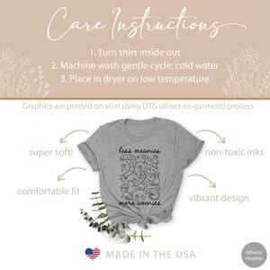Op de afbeelding: Athletic heather grijs t-shirt met de tekst "less meanies more weenies" en een zwarte hondenillustratie. Het shirt is gemaakt in de VS en bevat onderhoudsinstructies. Het wordt beschreven als superzacht, comfortabel en met een levendig ontwerp.