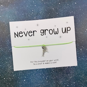 May include: A green string bracelet with a silver charm of a fairy. The card attached to the bracelet reads "Never grow up" and "Put this bracelet on your wrist, tie a knot & make a wish!"