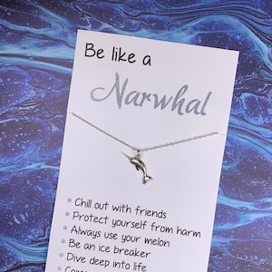 May include: A silver narwhal charm necklace with a white card that reads "Be like a Narwhal" and lists reasons to be like a narwhal, such as "Chill out with friends" and "Dive deep into life".