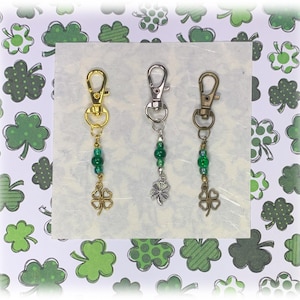 May include: Three gold, silver, and bronze keychains with green shamrock charms and green beads. The keychains are displayed on a white background with a green shamrock pattern.