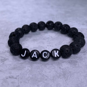 May include: Black lava rock beaded bracelet with white letter beads spelling the name "JACK".