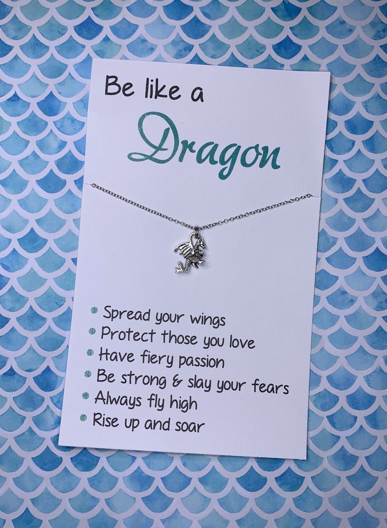 May include: A silver dragon charm necklace on a white card with the text "Be like a Dragon" and a list of inspirational phrases: "Spread your wings", "Protect those you love", "Have fiery passion", "Be strong & slay your fears", "Always fly high", "Rise up and soar".