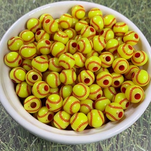 May include: A bowl filled with yellow and red softball-shaped beads. The beads have a red stitching design.