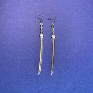 May include: A pair of silver sword-shaped earrings. The earrings are long and slender, with a detailed sword design.