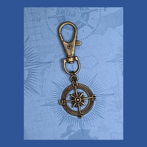 May include: A gold-toned compass keychain with a clip. The compass features a star in the center and the letters N, S, E, and W around the edge.