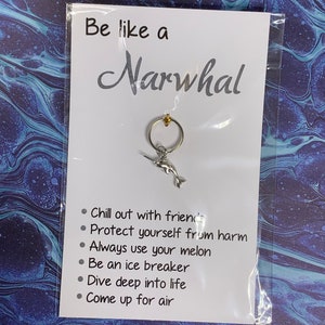 May include: A white card with the text "Be like a Narwhal" and a list of bullet points: "Chill out with friends", "Protect yourself from harm", "Always use your melon", "Be an ice breaker", "Dive deep into life", "Come up for air". A silver narwhal keychain is attached to the card.