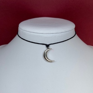 May include: A black choker necklace with a silver crescent moon pendant.