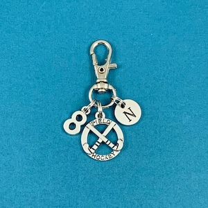 May include: Silver keychain with a hockey stick charm, a number 8 charm, and a charm with the letter N. The hockey stick charm has the words "Field Hockey" around it.