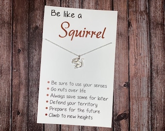May include: A white card with the text "Be like a Squirrel" in brown lettering. A silver necklace with a squirrel charm hangs from the card. The card lists six tips for being like a squirrel: "Be sure to use your senses", "Go nuts over life", "Always save some for later", "Defend your territory", "Prepare for the future", and "Climb to new heights".