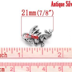 May include: Antique silver dragon charm, measuring 21 mm (7/8 inch) in size. The charm features a detailed dragon design with wings and a curled tail.