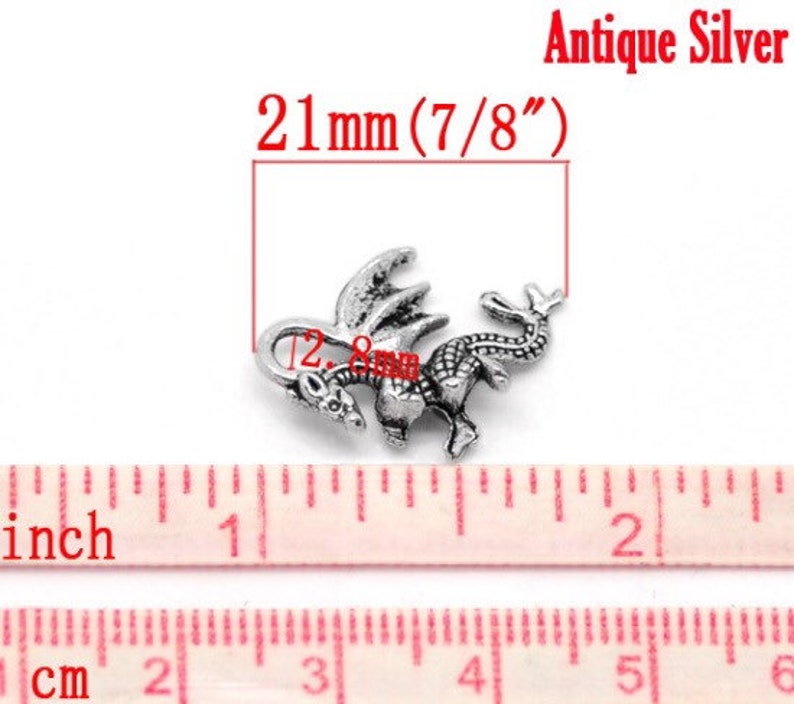 May include: Antique silver dragon charm, measuring 21 mm (7/8 inch) in size. The charm features a detailed dragon design with wings and a curled tail.