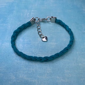 May include: A teal braided suede bracelet with a silver heart charm and a silver chain extender.