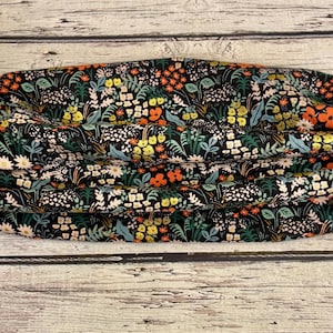 以下が含まれることがあります： 黒色の背景にオレンジ、黄色、白、青の花が咲き誇る、フローラル柄のヘアバンド。 中央でギャザーが寄せられ、テクスチャード加工が施されています。快適さを追求したデザインです。