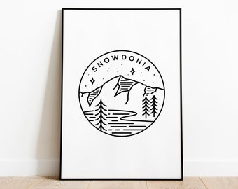 May include: Black and white line art print of a mountain range with the word "SNOWDONIA" in a circle around it. The print is on a white background and is framed in a black frame.