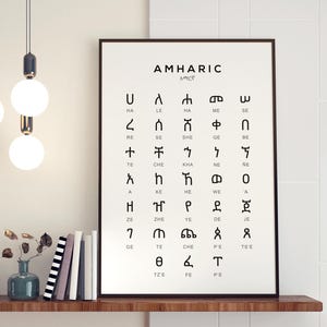 Puede incluir: Un cuadro enmarcado con el alfabeto amhárico en blanco y negro, expuesto en una estantería de madera. El póster presenta la escritura amhárica con transliteraciones en inglés. Hay libros y un jarrón en la estantería. Tres lámparas colgantes cuelgan.
