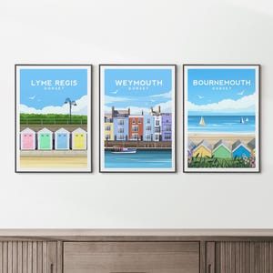 May include: Three framed travel posters featuring coastal scenes in Dorset. The first shows Lyme Regis beach huts, the second depicts Weymouth harbour buildings and a boat, and the third displays Bournemouth beach huts and sailboats on the water.