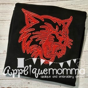 Könnte beinhalten: Schwarzes Sweatshirt mit einem roten, glitzernden Wildkatzenkopf-Design. Der Text "Appelquemomma applique and embroidery designs" befindet sich am unteren Bildrand.