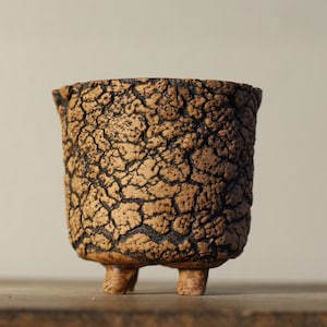 Può includere: Un piccolo vaso in ceramica marrone con una glassa craquelé e tre gambe.