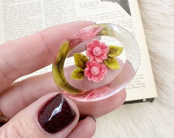 Broche de resina ovalada con intaglio invertido y flores de color rosa dulce.