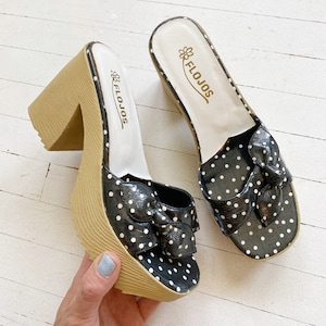 May include: A pair of black and white polka dot platform sandals with a bow detail. The sandals are made by the brand "Flojos".