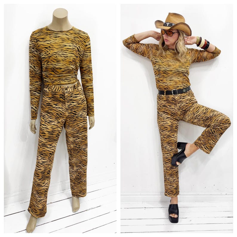 May include: A two-piece set featuring a long-sleeved top and pants with a tiger stripe pattern in shades of brown and black. The outfit is displayed on a mannequin and modeled by a person wearing a cowboy hat, sunglasses, and black shoes.