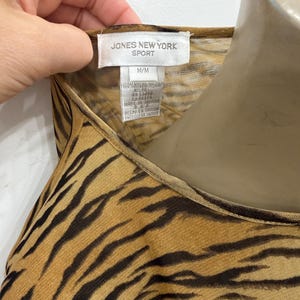 May include: A close-up of a sleeveless top with a tiger stripe pattern in shades of brown and black. The tag reads "JONES NEW YORK SPORT" and "M/M". The fabric is 100% nylon.