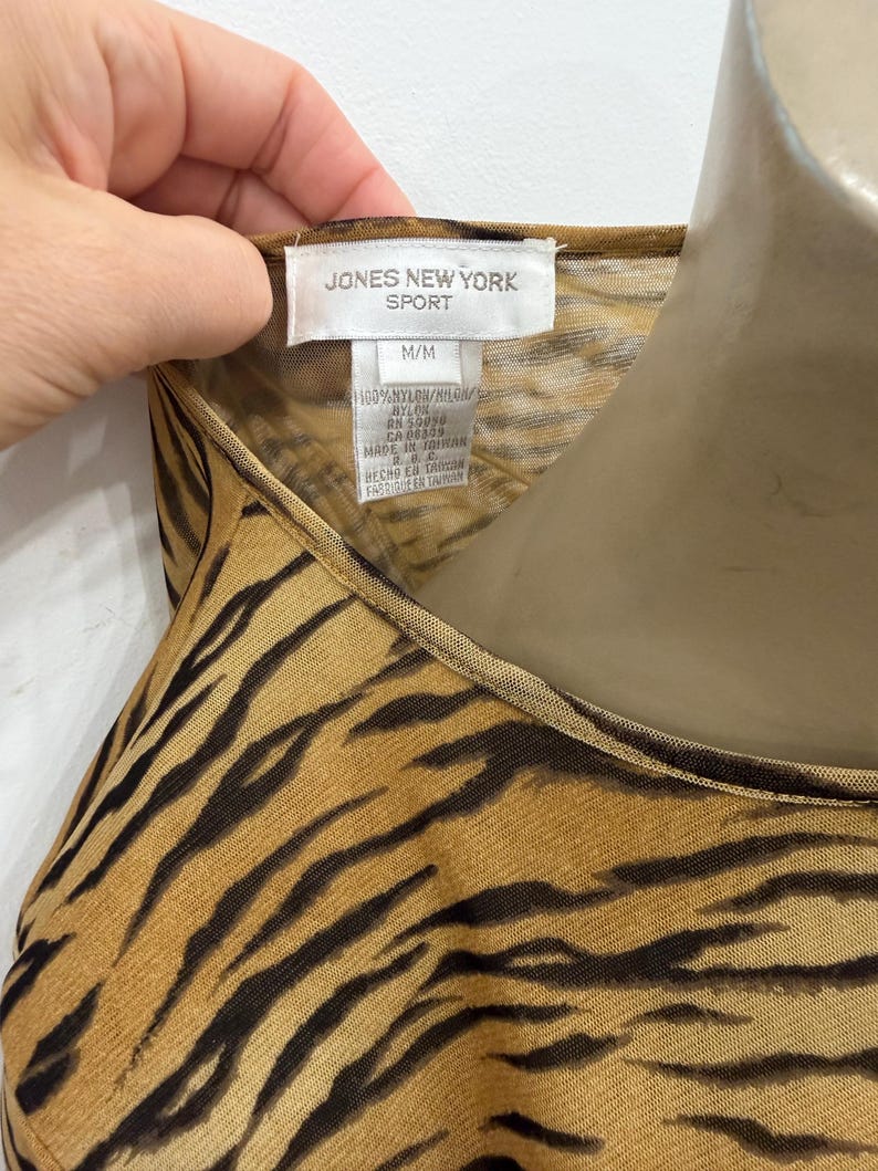 May include: A close-up of a sleeveless top with a tiger stripe pattern in shades of brown and black. The tag reads "JONES NEW YORK SPORT" and "M/M". The fabric is 100% nylon.