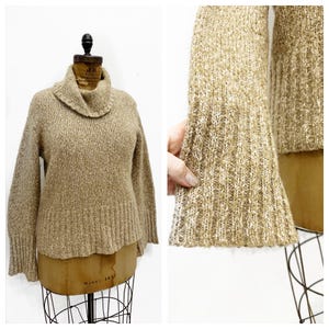 May include: A beige turtleneck sweater with a ribbed texture and long sleeves. The sweater has a slightly cropped length and a relaxed fit.