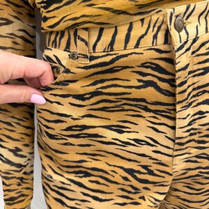 May include: A two-piece outfit featuring a tiger stripe pattern in shades of tan and black. The outfit includes a long-sleeved top and pants. The pants have a button and pocket detail. The fabric appears to be a soft, lightweight material.