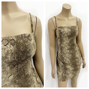 Peut inclure: Une robe courte sans manches avec un motif peau de serpent dans des tons marron et beige. Le vêtement présente une encolure droite, de fines bretelles et une coupe ajustée arrivant à mi-cuisse, mettant en valeur une texture reptilienne.