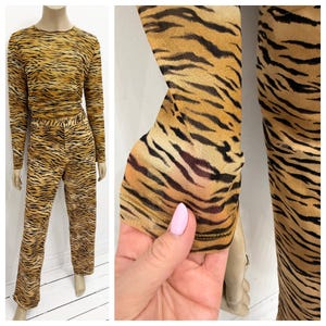 May include: A two-piece set featuring a long-sleeved top and pants. The outfit has a tiger stripe pattern in shades of brown and black. The fabric appears to be sheer and lightweight, with a close-up showing the sleeve detail.