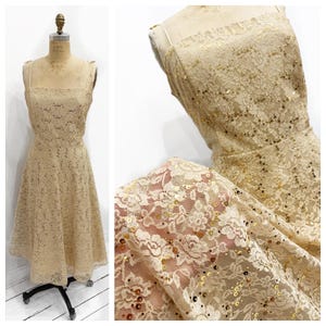 May include: A vintage beige lace dress with a square neckline and a midi-length skirt. The dress is embellished with gold sequins and is displayed on a mannequin. The lace pattern features floral designs.