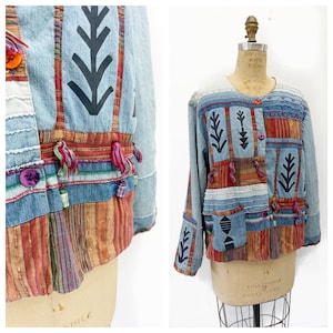 Peut inclure: Une veste en jean à manches longues avec un design en patchwork composé de panneaux en tissu rayé multicolore, d'appliques noires en forme de flèche, de pompons en fil suspendus et de divers boutons colorés. Col rond et poche avant.