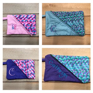 May include: Four zippered pouches with a mermaid scale pattern. The pouches are in different colors: pink, blue, purple, and teal. Each pouch has a different embroidered design: "CNF", a cursive "C", a cursive "C", and the name "Cathryn".