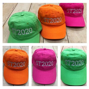 May include: Three baseball caps in different colors: orange, pink, and green. Each cap has the text "ST2020" embroidered on the front in white.