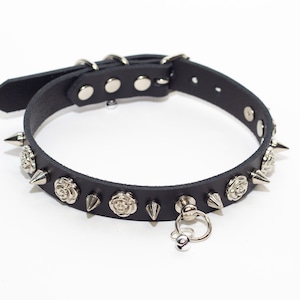 Peut inclure: Collier en cuir noir avec des accents de roses et de pointes argentés. Le collier a un charme de cloche argentée attaché à un anneau en D.