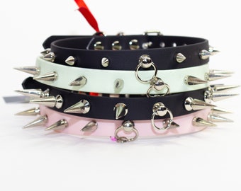 May include: Three spiked collars in black, white and pink with silver hardware and rings. The collars are stacked on top of each other.