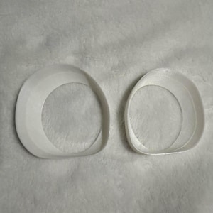 May include: Two white, oval-shaped objects with a rounded, raised edge. The objects are positioned side-by-side against a soft, white background. The design is simple and minimalist, with a focus on the form and shape.