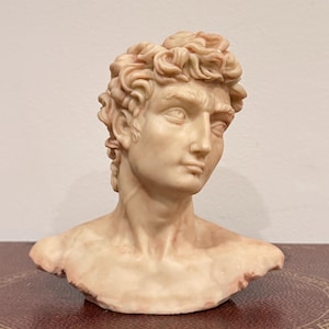 May include: A white marble bust sculpture of a man with short curly hair. The sculpture is detailed and realistic, with a focus on the man's face.