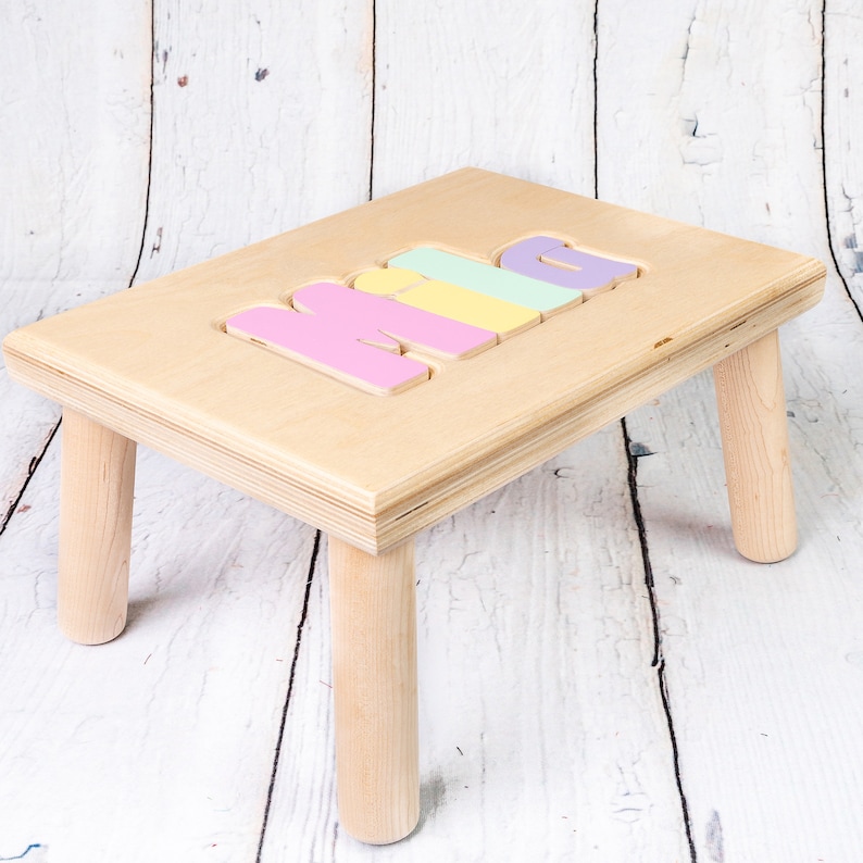 May include: A wooden step stool with four legs and the word "MIA" spelled out in colorful letters on the top.