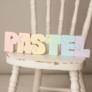 Op de afbeelding: Pastelkleurige houten puzzelstukjes die het woord "PASTEL" spellen.
