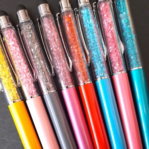 May include: A set of ten colourful pens with clear barrels filled with colourful crystals. The pens have silver caps and a silver stylus tip.