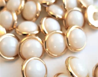 May include: A pile of white pearl buttons with gold metal rims. The buttons are round and have a smooth, glossy finish.